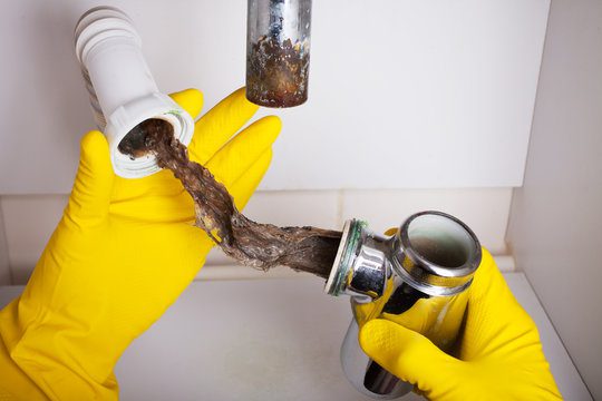 Plumber cleaning clogged drain pipe with wrench and gloves