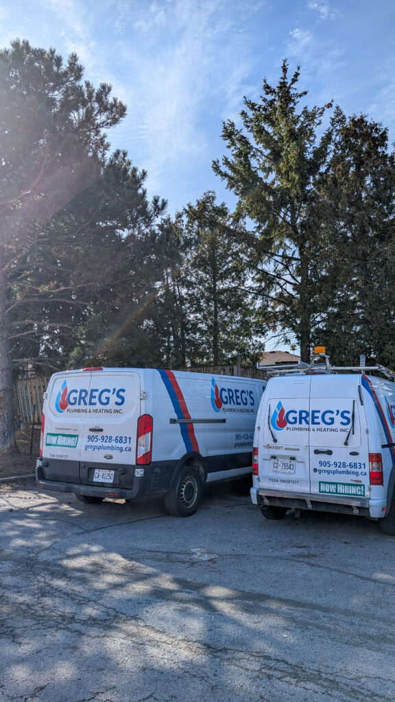 Greg’s Plumbing and Heating vans parked near a job site