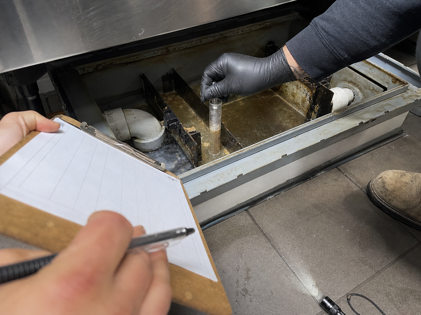 Plumber measuring grease levels inside a commercial interceptor for compliance reporting